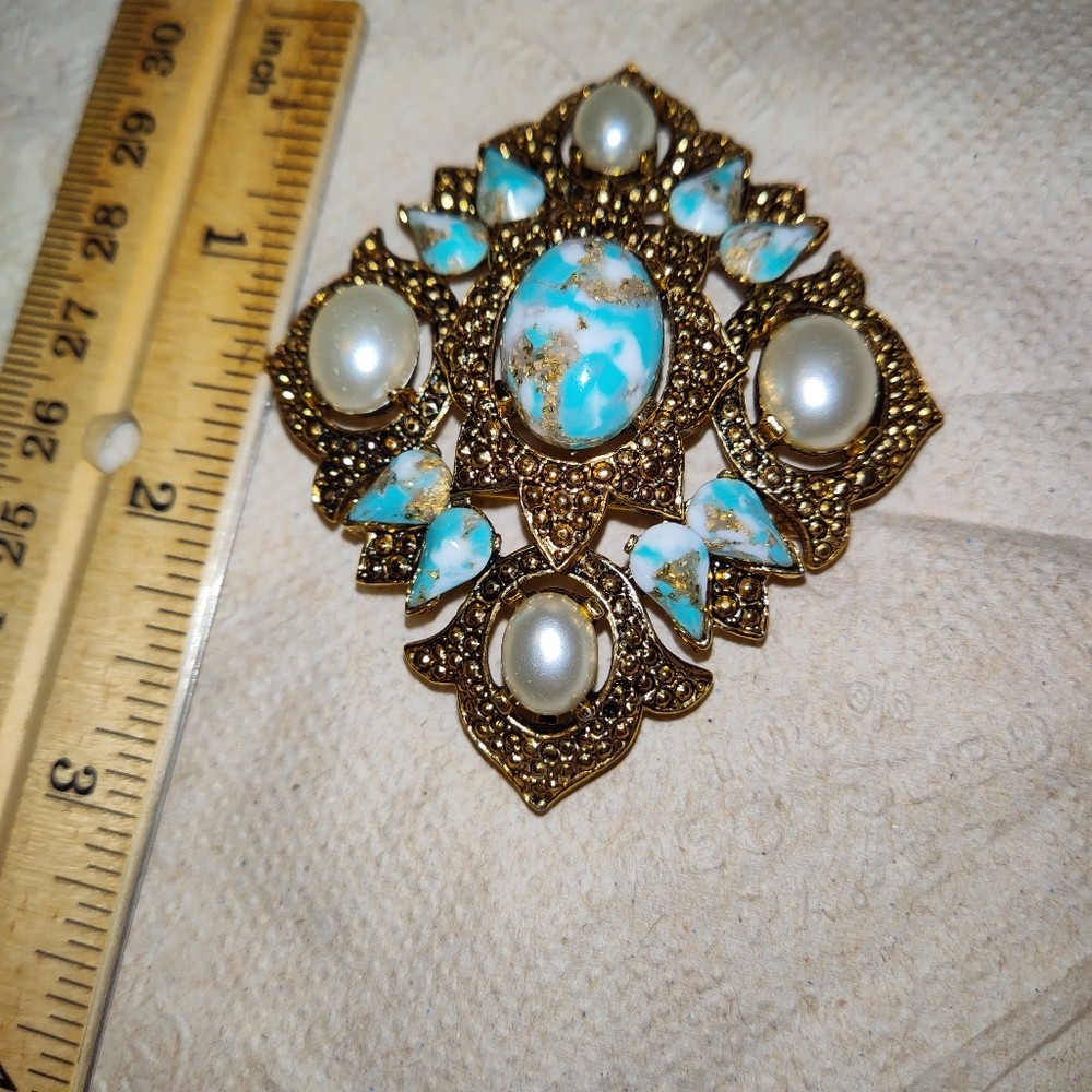 A gold tone brooch faux pearl, blue, gold, and white color on the stones